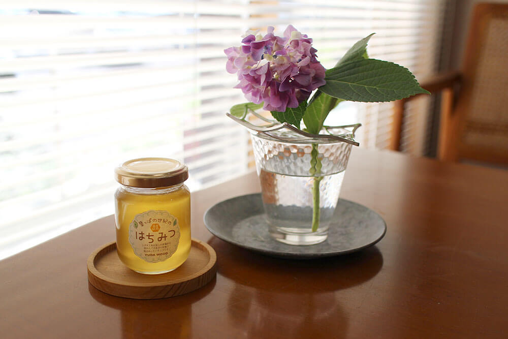 応接テーブルの窓辺の写真。紫陽花の小さな花と新ハチミツの小瓶